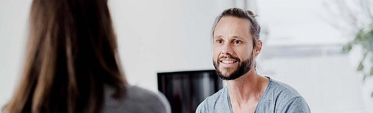 Zwei Menschen miteinander im Gespräch, eine Person ist nur von hinten zu sehen